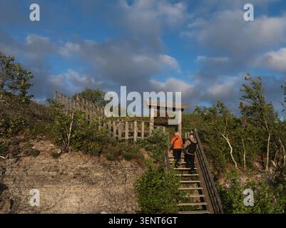 Jeune actif avec des sacs à dos grimpant les escaliers en bois sur un sentier de falaise calcaire lors d'une randonnée estivale. Banque D'Images