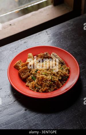 Riz frit fait maison ou nasi goreng sur assiette rouge avec beaucoup de garnitures telles que : tofu, poisson, poulet, légumes et tempeh. Véritable nourriture de réconfort Banque D'Images
