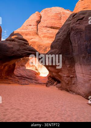 Une arche à la sortie d'une vallée cachée au sol sablonneux parmi d'énormes rochers dans le parc national d'Arches, Moan, Utah Banque D'Images
