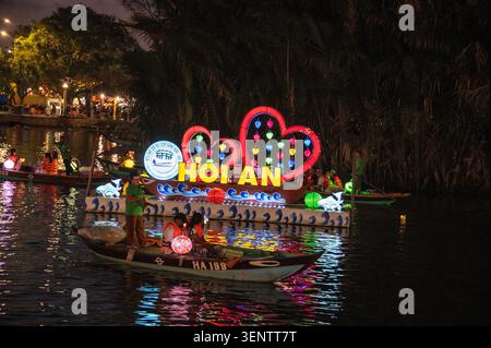 Les bateaux flottent devant une île flottante éclairée sur la rivière Thu bon à Hoi an. Hoi an est célèbre pour sa flottille nocturne de sampans (bateaux à fond plat) avec Banque D'Images