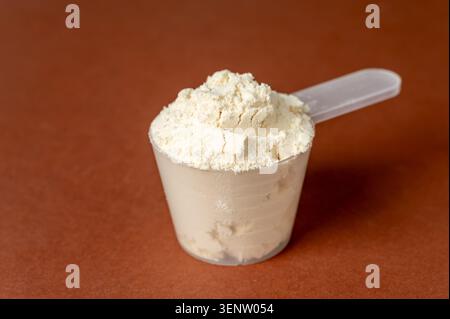 Cuillère à mesurer avec de la poudre de protéines sur fond brun, nutrition sportive et supplément Banque D'Images