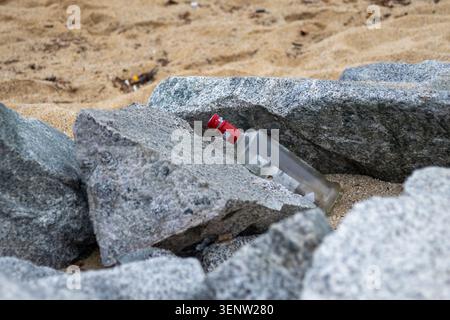 Photographie rapprochée d'une bouteille de verre jetée partiellement enterrée parmi les rochers côtiers et le sable. Image de l'environnement mettant en évidence les déchets, accumulateurs de déchets Banque D'Images