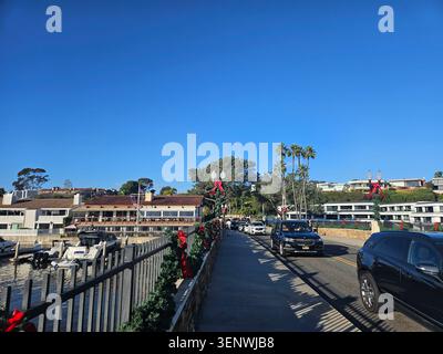 Scène portuaire calme à Balboa Island à Newport Beach, Californie, avec des bateaux amarrés, des maisons en bord de mer, des palmiers, reflets du soleil sur l'eau, et a Banque D'Images
