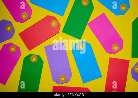 Gros plan d'un groupe d'étiquettes de prix en carton multicolores pour la vente au détail sur une table jaune. Banque D'Images