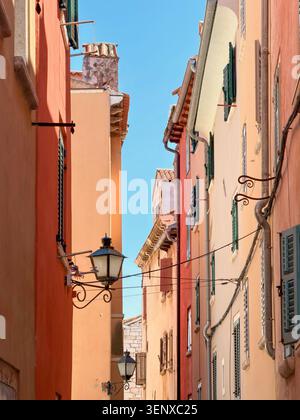 Étroite rue pavée bordée de bâtiments colorés orange et rose dans la vieille ville de Rovinj, Croatie. Banque D'Images