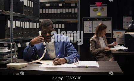 Black COP mène une enquête discrète, analyse les preuves et fait des appels téléphoniques importants. Banque D'Images