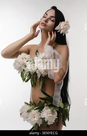 Une femme aux longs cheveux bruns pose gracieusement, ornée de fleurs vibrantes, embrassant la beauté de la nature Banque D'Images
