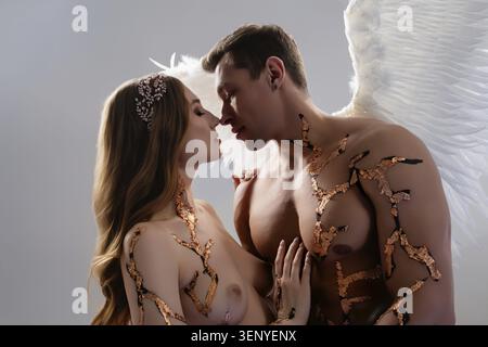 Un couple partage un moment tendre, orné d'ailes d'ange et d'art corporel complexe, capturé dans un éclairage doux Banque D'Images
