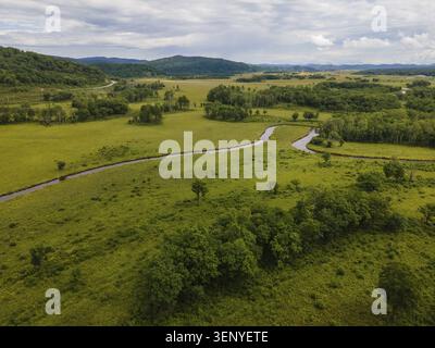 De vastes champs verts s'étendent à travers le paysage de Vladivostok, en Russie, avec une rivière sinueuse coupant à travers la terre. Le feuillage luxuriant reflète le BE Banque D'Images