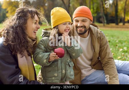 Les parents apprécient le pique-nique d'automne tandis que leur fille sourit et tient la pomme dans le parc ensemble Banque D'Images