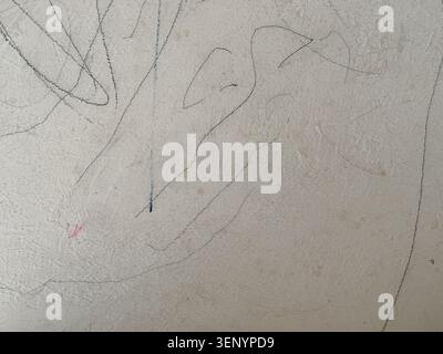 Un gros plan d'un mur texturé beige clair recouvert de griffonnages aléatoires faits à l'aide de crayons. Banque D'Images