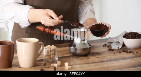 Personne préparant du café frais avec des grains moulus et cezve sur une table en bois avec des cubes de sucre et des tasses Banque D'Images