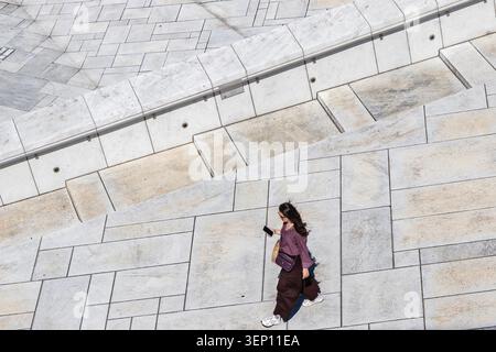 Vue en grand angle d'une femme marchant sur le toit en marbre de l'Opéra d'Oslo en Norvège tenant un smartphone et portant un sac à bandoulière Banque D'Images
