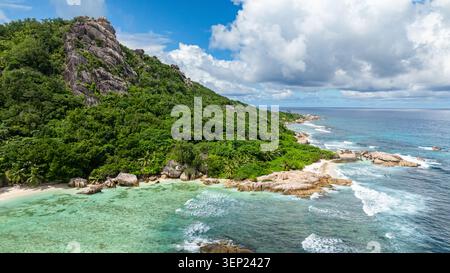 Formations rocheuses massives couvertes de verdure, entourées d'eaux turquoises claires sous un ciel bleu. Seychelles, la Digue. Banque D'Images