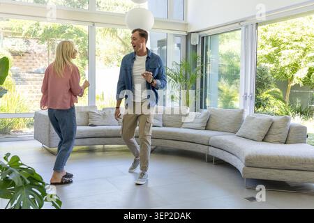Couple dans des vêtements décontractés marcher et parler dans le salon moderne par canapé incurvé et fenêtres Banque D'Images