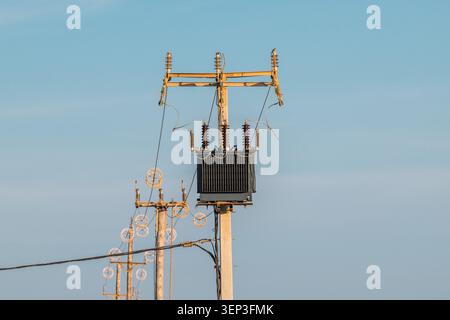Transformateur de puissance monté sur poteau de service avec lignes de distribution électrique contre le ciel bleu clair Banque D'Images