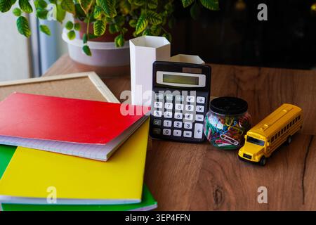 Jouet d'autobus scolaire jaune avec calculatrice blocs-notes marqueurs et trombones sur la table en bois crée une scène de bureau de retour à l'école pour l'apprentissage des mathématiques en classe Banque D'Images