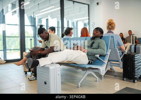 Les passagers se détendent et utilisent leur smartphone pendant qu'ils attendent dans le hall d'entrée d'un terminal d'aéroport Banque D'Images