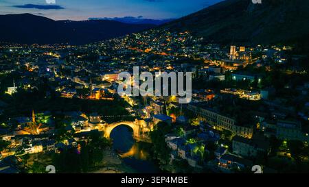 Mostar, Bosnie-Herzégovine 7 juin 2026 Panorama aérien de Mostar au crépuscule avec le Vieux Pont, le centre historique et les gratte-ciel illuminés de la ville. Banque D'Images