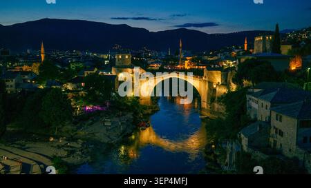 Mostar, Bosnie-Herzégovine 7 juin 2026 vue en soirée surélevée du Vieux Pont et du quartier historique illuminé au-dessus de la rivière Neretva. Banque D'Images