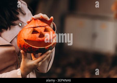 Gros plan d'une jeune fille tenant une lanterne de citrouille sculptée à l'extérieur pendant la célébration d'Halloween avec une ambiance automnale chaude et effrayante de la saison de décor ou de friandise Banque D'Images