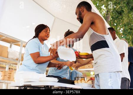 Jeune femme noire aidant les nécessiteux par le biais de dons alimentaires et de bénévolat dans un programme de sensibilisation communautaire. Les travailleurs caritatifs de Food Drive partagent des produits frais et des produits de première nécessité aux pauvres et aux sans-abri. Banque D'Images