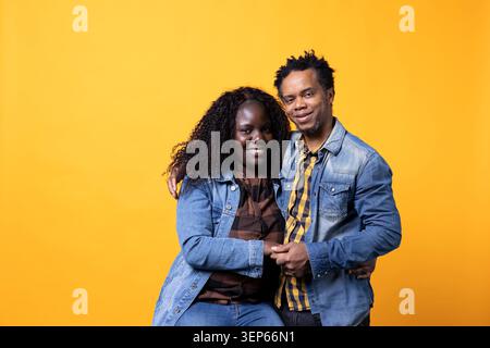 Joyeuses âmes afro-américaines s'embrassant en studio, souriant et se sentant reconnaissantes sur fond jaune tandis que positif couple marié chanceux embrassant avec passion, montrant de la gratitude. Banque D'Images
