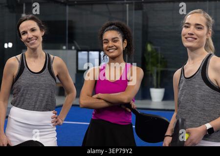 Trois amies se tenant sur le terrain bleu à l'intérieur de la salle de gym portant des débardeurs, tenant des pagaies, balle Banque D'Images