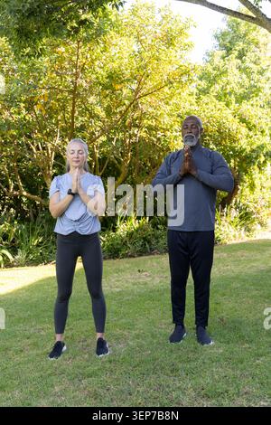 Couple en appuyant les mains à la poitrine, debout dans le jardin ensoleillé, femme portant le tracker de poignet et des baskets Banque D'Images