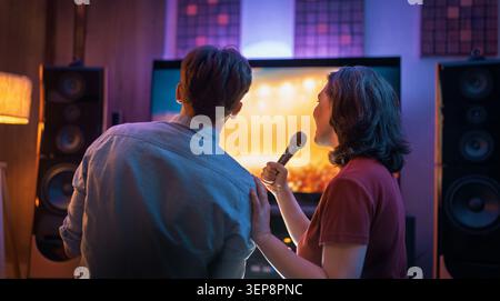 Moment de style de vie chaleureux et joyeux comme un couple profite d'une soirée karaoké à la maison. Immergés dans la musique, ils se lient sur un amour partagé pour le chant, le rire, un Banque D'Images