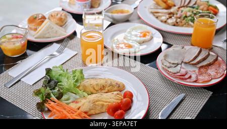 Un copieux petit-déjeuner buffet composé d'omelettes, d'œufs au plat, de jus d'orange frais, de charcuterie et de pâtisseries est servi sur une table moderne. Un concept de lu Banque D'Images
