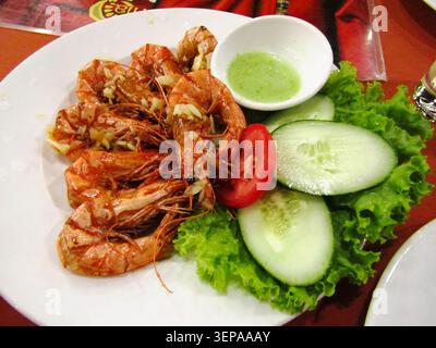 Assiette de crevettes tigrées frites à l'ail, servies avec tranches de concombre fraîches, tomate et sauce verte. Affûtage sélectif Banque D'Images
