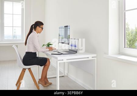 Femme d'affaires examinant les analyses au bureau à domicile lumineux à l'aide d'un ordinateur et d'un ordinateur portable Banque D'Images