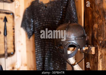 Casque médiéval en métal monté sur support en bois avec armure de mailles accrochée à l'arrière-plan, montré à l'intérieur chaud intérieur rustique en bois avec peu de profondeur Banque D'Images
