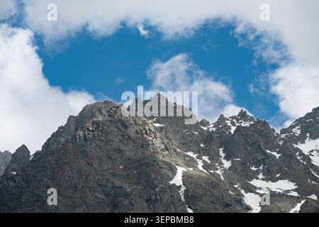 Majestueux sommets de montagnes rocheuses avec des restes de neige sous un ciel nuageux bleu, paysage sauvage alpin . Hautes crêtes de montagne acérées et falaises avec sn Banque D'Images