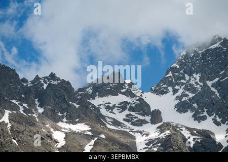 Majestueuses montagnes rocheuses couvertes de neige sous ciel bleu et nuages. Vue panoramique sur les falaises recouvertes de neige dans les hautes terres avec ciel nuageux. Banque D'Images