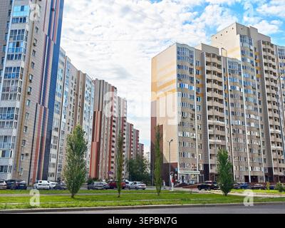 Orenburg, Russie - 22 août 2025 : plusieurs immeubles d'appartements se tiennent côte à côte le long d'une rue avec des voitures garées à proximité sous un ciel bleu avec des nuages Banque D'Images