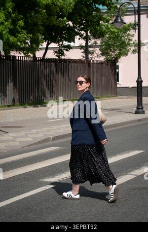 Jeune femme en lunettes de soleil traverse le passage piétonnier sur la rue calme de la ville. Marketing urbain, contenu de mobilité urbaine, publicité de voyage Banque D'Images