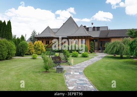 Maison en bois maison en rondins avec beau toit carrelé dans la campagne domaine dans le parc. Jardin paysager exquis avec chemin pavé en pierre et Banque D'Images
