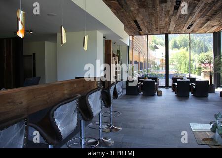 Photographie intérieure éditoriale d'un salon d'hôtel contemporain au Tyrol, en Autriche. L'espace dispose d'un comptoir de bar rustique en bois, tabourets de bar design avec Banque D'Images