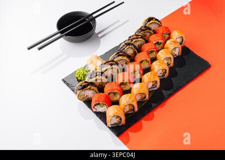 Un grand plateau contient différents types de rouleaux de sushi. Les sushis sont soigneusement disposés avec du wasabi et du gingembre sur le côté. Les baguettes sont placées au-dessus du plateau prêt à l'emploi. Banque D'Images
