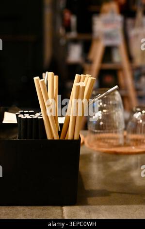 Plan vertical détaillé d'un organisateur de comptoir noir rempli de pailles écologiques dans un bar faiblement éclairé. La composition Banque D'Images