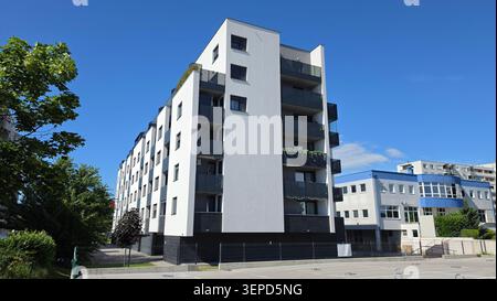 Un complexe résidentiel contemporain d'appartements à plusieurs étages, doté d'une façade blanche, de balcons noirs et d'une base sombre, jouxte un asphalte Banque D'Images