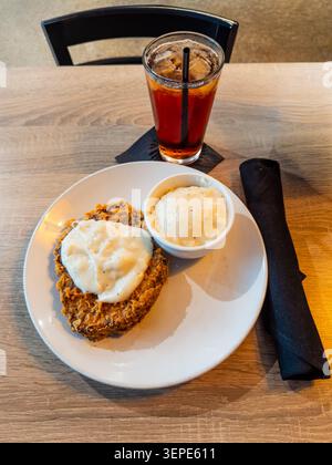 Assiette blanche contient un steak pané frit de campagne avec une sauce crémeuse. Le petit bol contient un plat d'accompagnement. Grand verre à thé glacé avec une paille se trouve à proximité. Banque D'Images