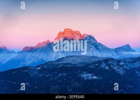 Majestueux pic de montagne Dolomites baigné dans alpenglow vibrant au lever du soleil contre un ciel rose et bleu doux avec des crêtes stratifiées et brumeux à l'Italie Banque D'Images