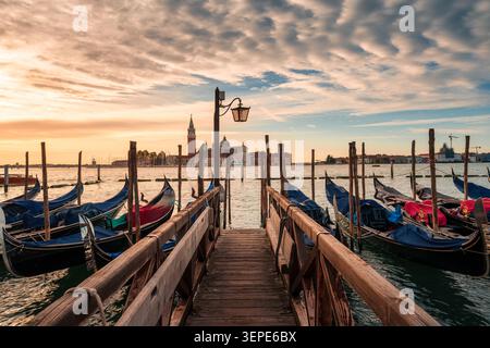 Vue panoramique de la jetée en bois surplombant les gondoles vénitiennes classiques sur le grand canal avec l'église de San Giorgio Maggiore pendant le matin doré à Venise, I. Banque D'Images