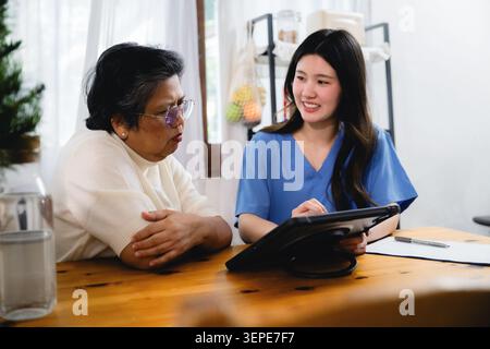 Infirmière asiatique souriante expliquant la tablette numérique femme âgée sérieuse, soignant à domicile consultant la tablette pour patients âgés, expliquant la médecine Banque D'Images