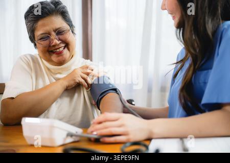 Femme aînée asiatique recevant un médecin de contrôle de la pression artérielle alors que la jeune infirmière utilisant le sphygmomanomètre numérique senior, gériatrique service de soins infirmiers routi Banque D'Images