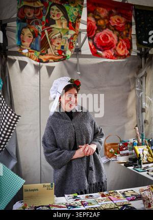 Une commerçante en costume médiéval se tient à un stand d'artisanat pendant le marché médiéval de Tallinn dans la vieille ville de Tallinn, Estonie, le 11 juillet 2025. Banque D'Images
