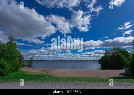 Vue panoramique sur une plage de sable au bord d'un lac à Tampere. Le rivage étendu est encadré par des arbres et des buissons verdoyants sous un ciel bleu vif Banque D'Images